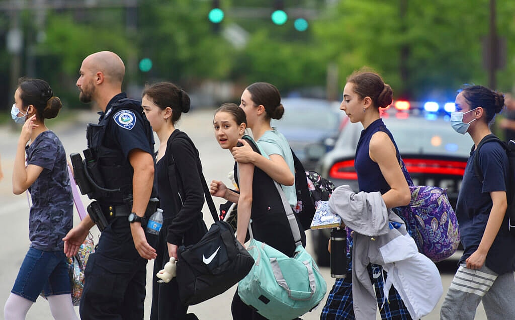 Police escort a group of women across the street in front of a police car