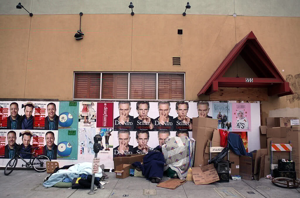 Homeless people sleep on the sidewalk in front of closed restaurant