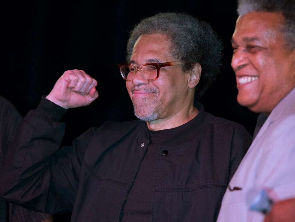 Former prisoner Albert Woodfox pumps his fist, wearing a black shirt and jacket