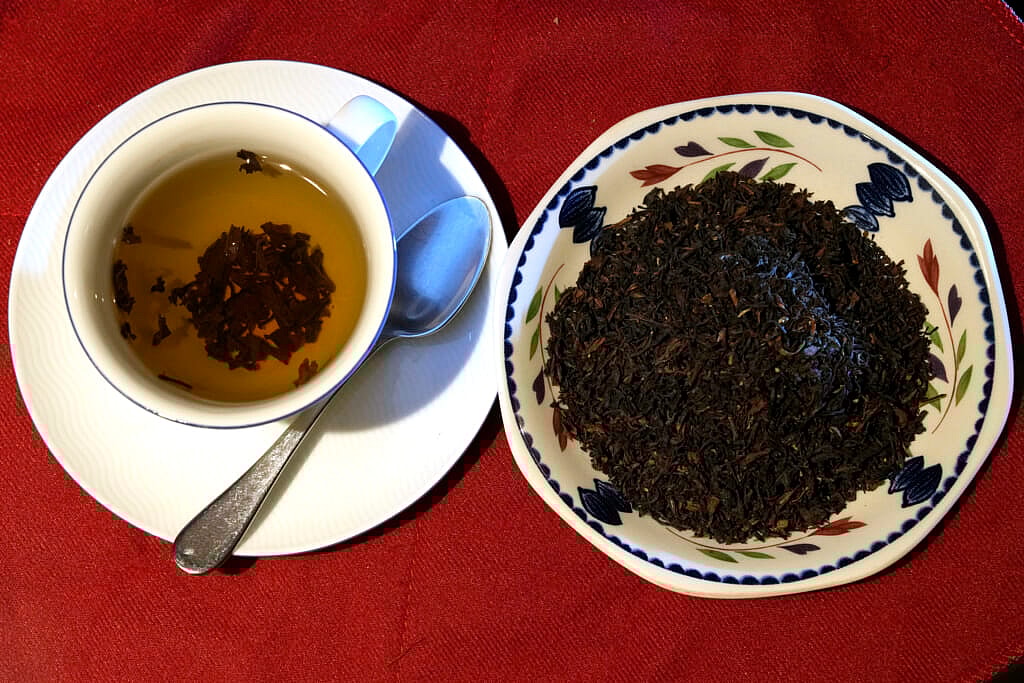 A cup of black tea with a spoon and tea leaves
