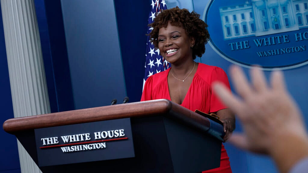 White House press secretary Karine Jean-Pierre, wearing a red dress, stands behind a podium