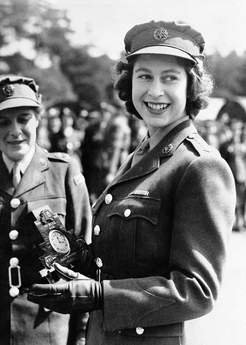 Black-and-white photo of Britain's Queen Elizabeth II as a young woman in her military uniform, holding a clock