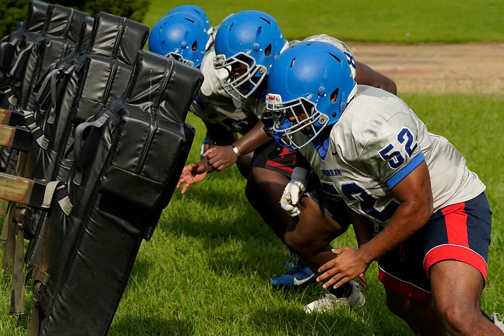 Murrah High School football offensive linemen wearing blue helmets square up against the blocking sled at practice