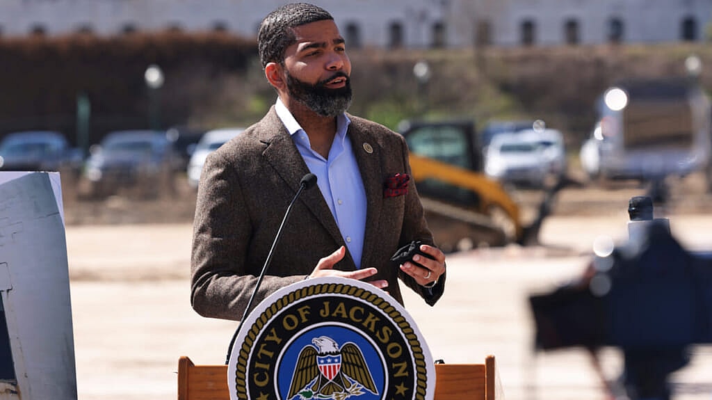 Jackson, Mississippi, Mayor Chokwe Antar Lumumba behind a podium wearing a brown jacket and light blue shirt