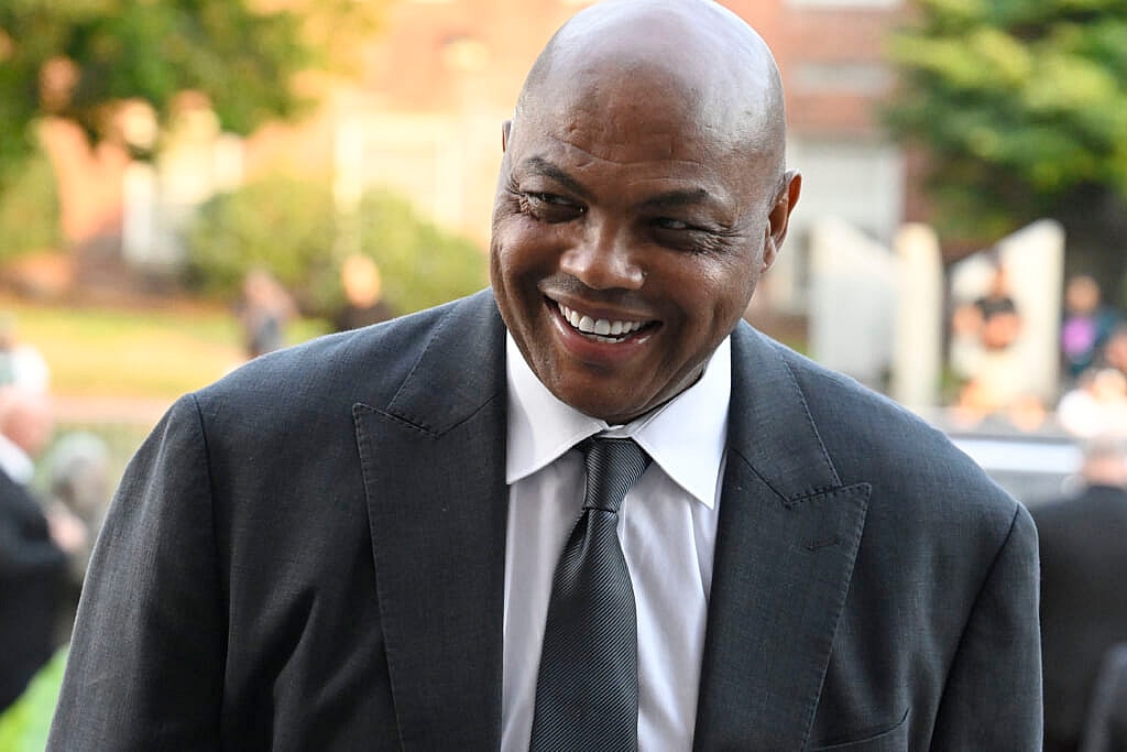 Charles Barkley, wearing a gray suit, white shirt and gray tie, smiles while standing outside