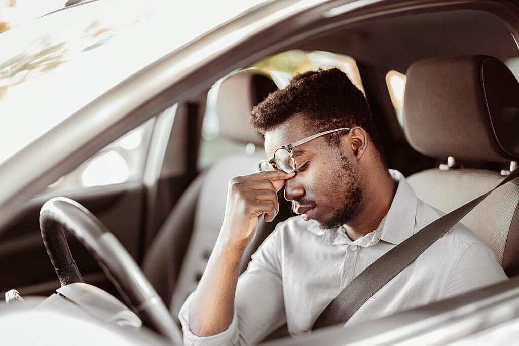 A man sitting in a car holding the bridge of his nose