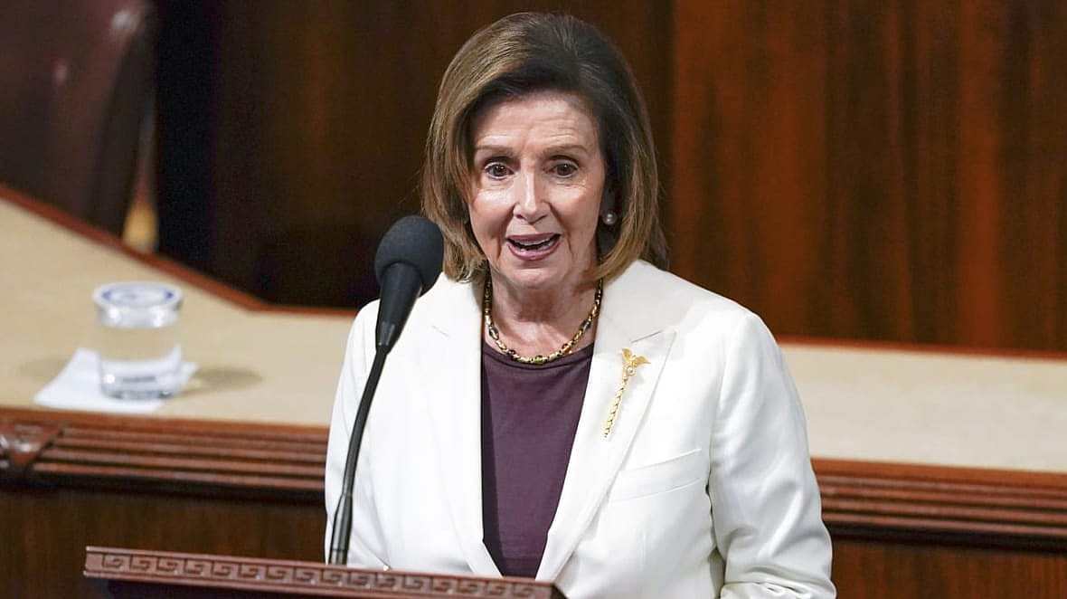 Former House Speaker Nancy Pelosi of California behind a podium wearing a white jacket and purple top