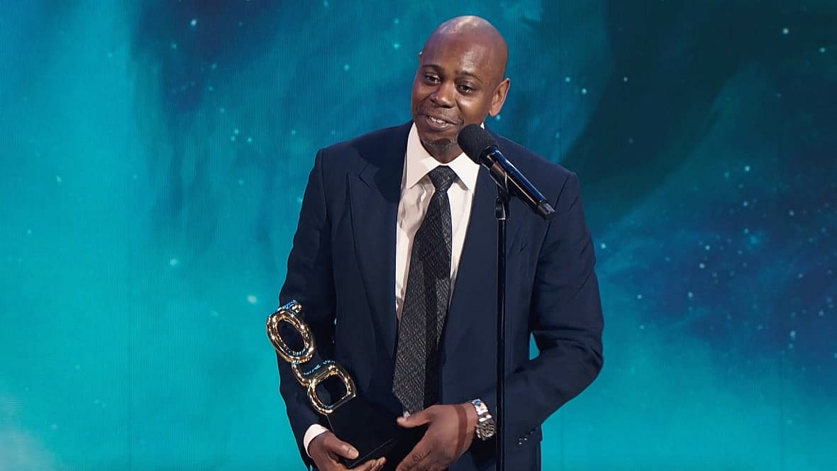 Comedian Dave Chappelle holds his trophy at theGrio awards ceremony, wearing a dark blue jacket and black tie