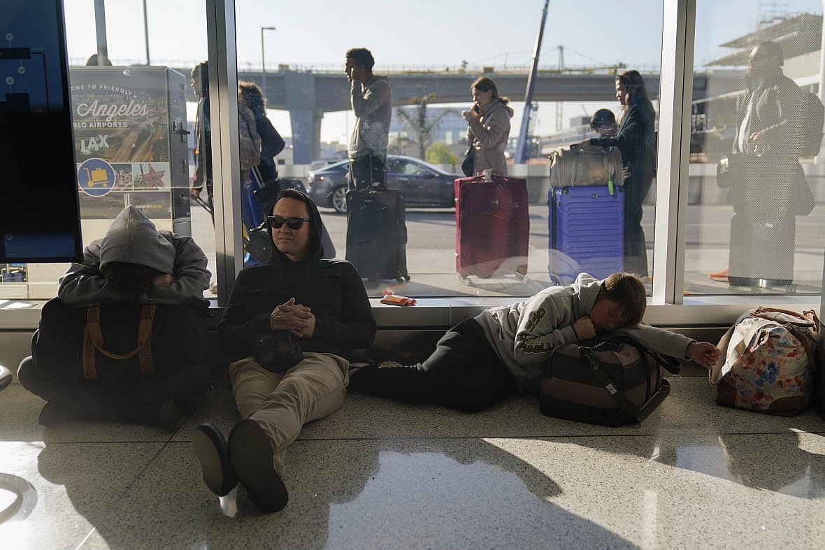 Rome DeGuzman sits on the floor of an airport terminal next to his two sons