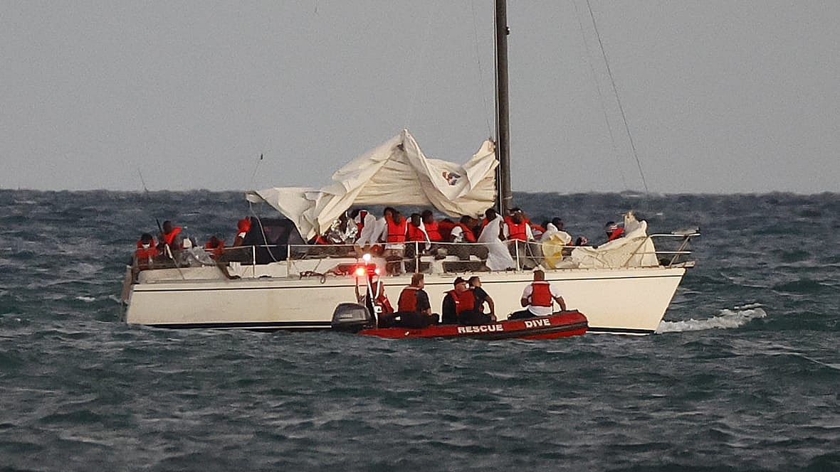 U.S. Coast Guard members pull up alongside a sailboat carrying a large group of migrants