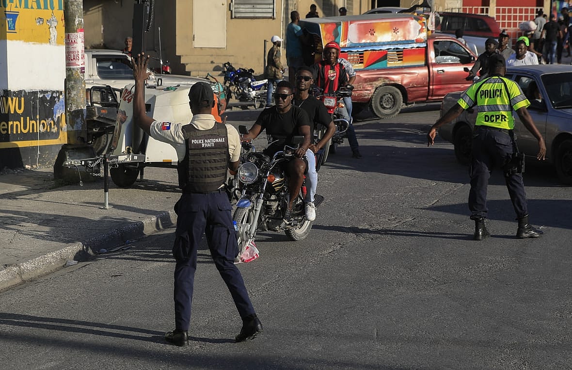 A national police officer gestures to a motorcyclist and passenger on a street in Haiti