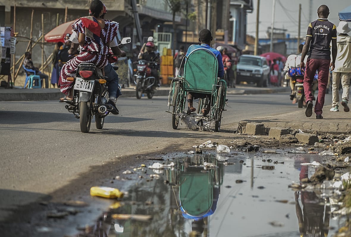 Paul Mitemberezi in a green three-wheeled wheelchair drives down a city street next to a motorcycle