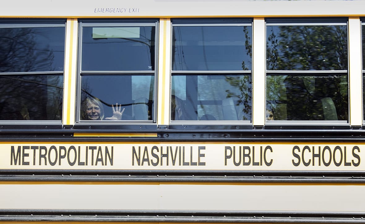 A crying child presses their hand against the window of a bus marked Metropolitan Nashville Public Schools