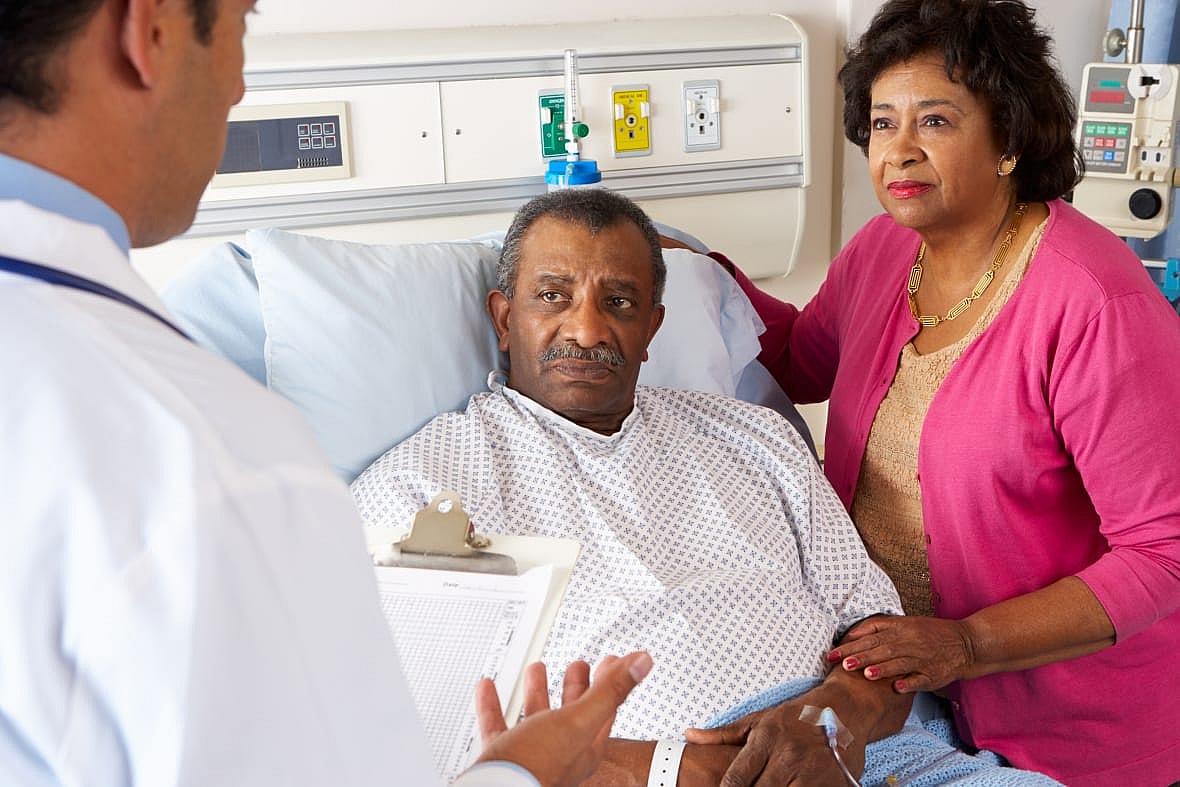 A doctor speaks to a man in a hospital bed and his wife