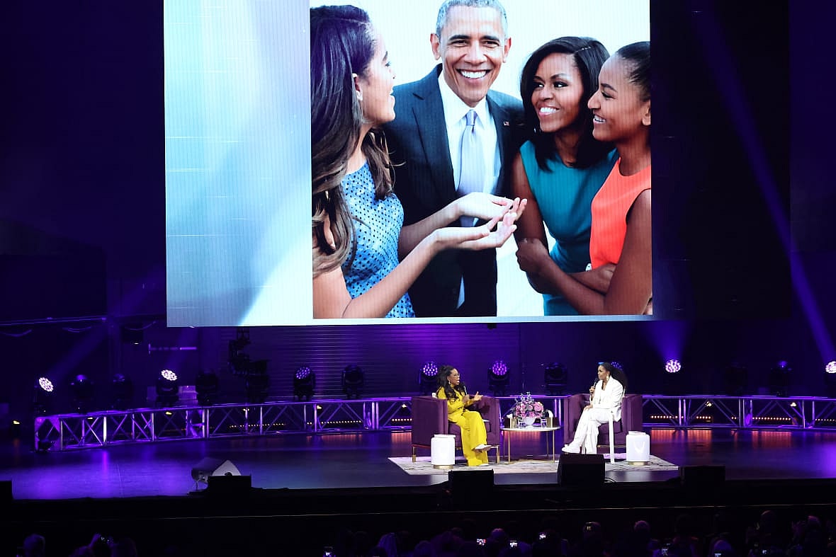 TV personality Oprah Winfrey and former First Lady Michelle Obama on stage before a screen showing the Obama family