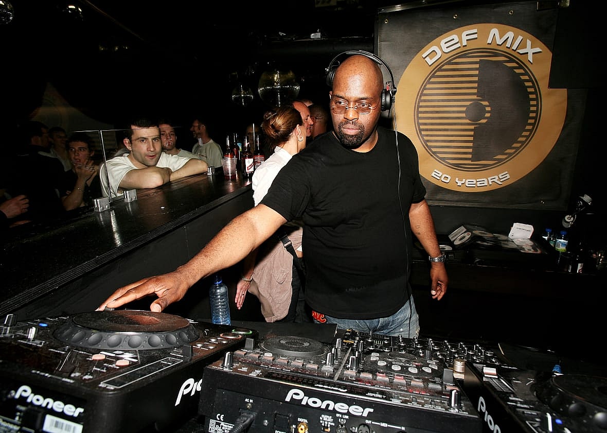 DJ Frankie Knuckles performing on a mixing deck wearing a black shirt and headphones