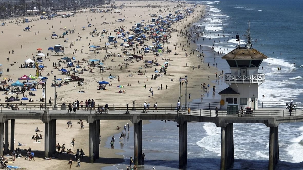 Beach-goers flock to the shore south of the pier in Huntington Beach, California