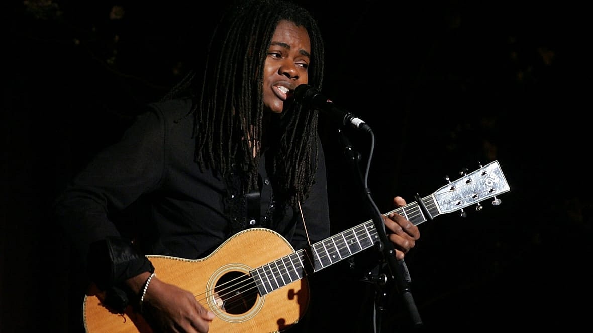 Singer-songwriter Tracy Chapman at a microphone holding an acoustic guitar