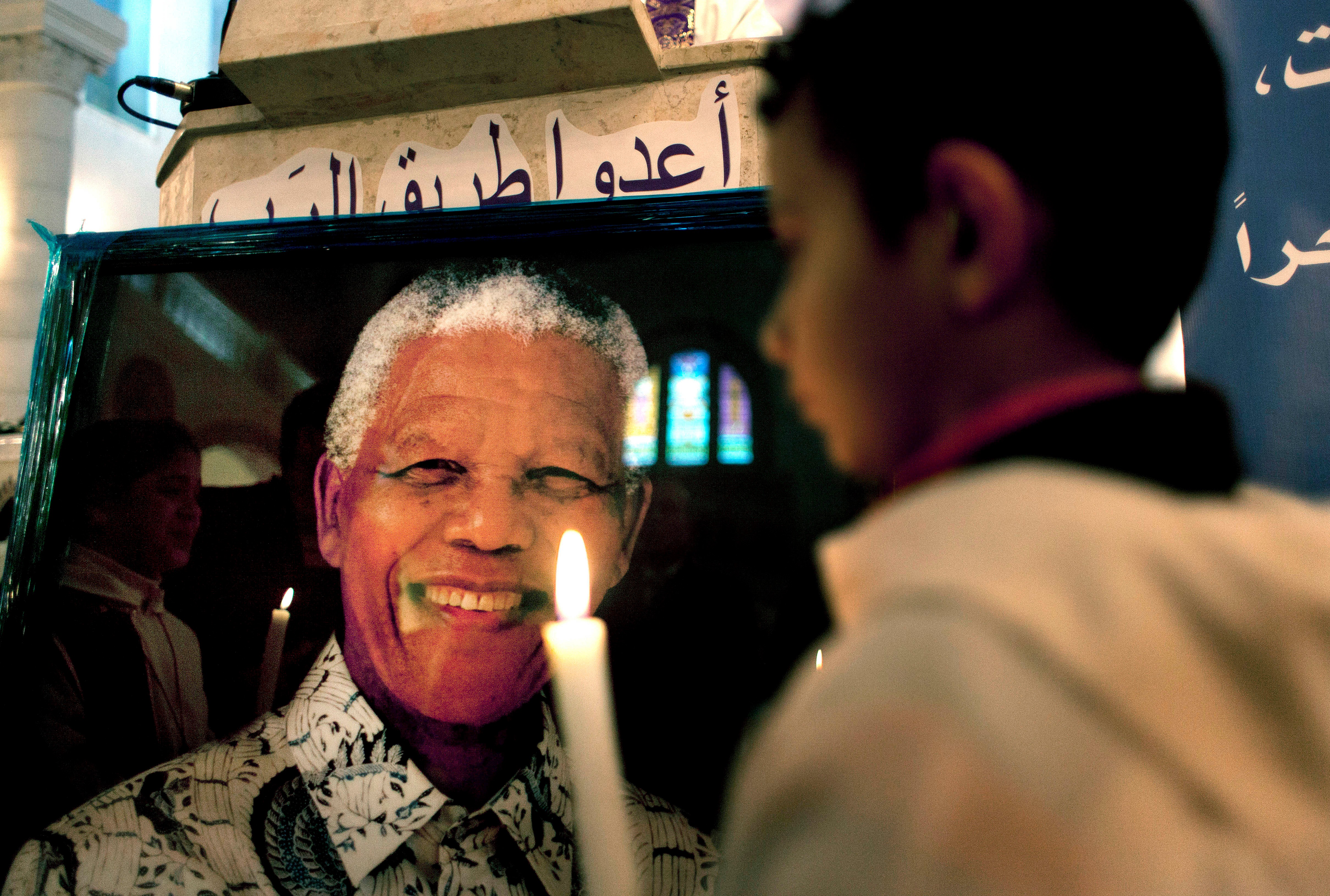 A Palestinian child holds a lit candle as he prays in front of a poster of late South African leader Nelson Mandela
