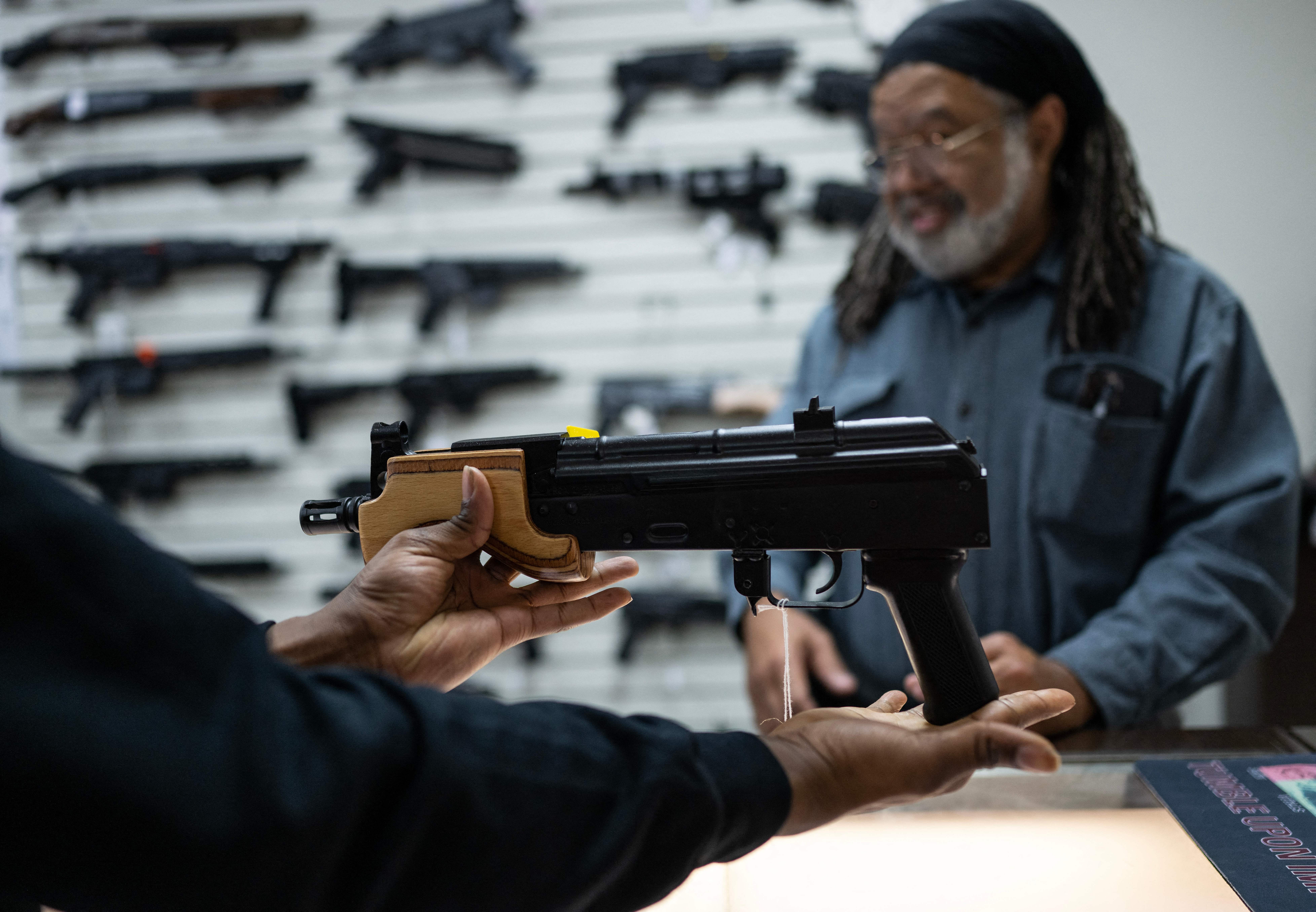 Earl J. Brake, Sr., owner of EJB's Gun Shop, shows a gun to a customer