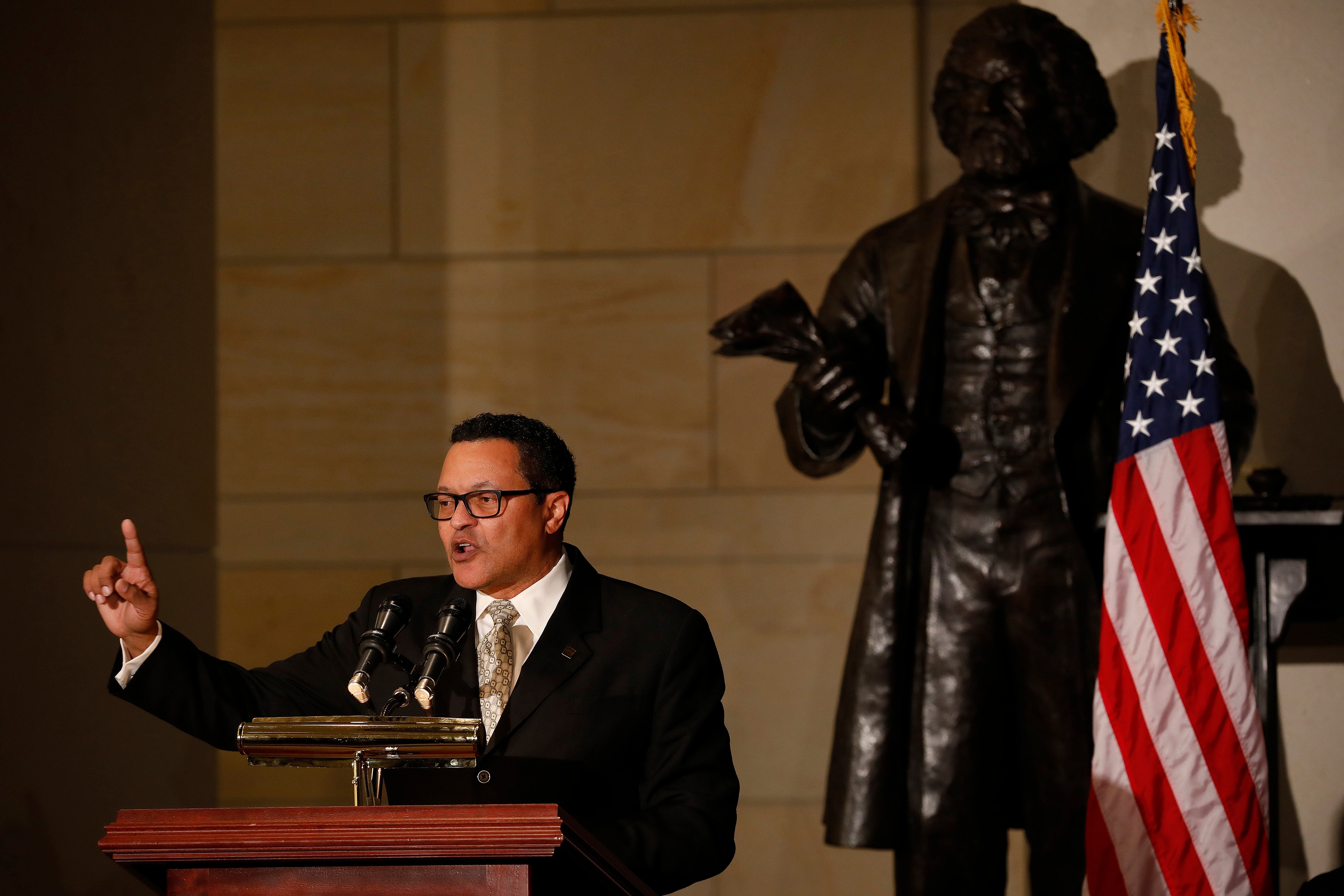 Ken Morris, a descendant of Frederick Douglass, speaks behind a podium wearing a black coat