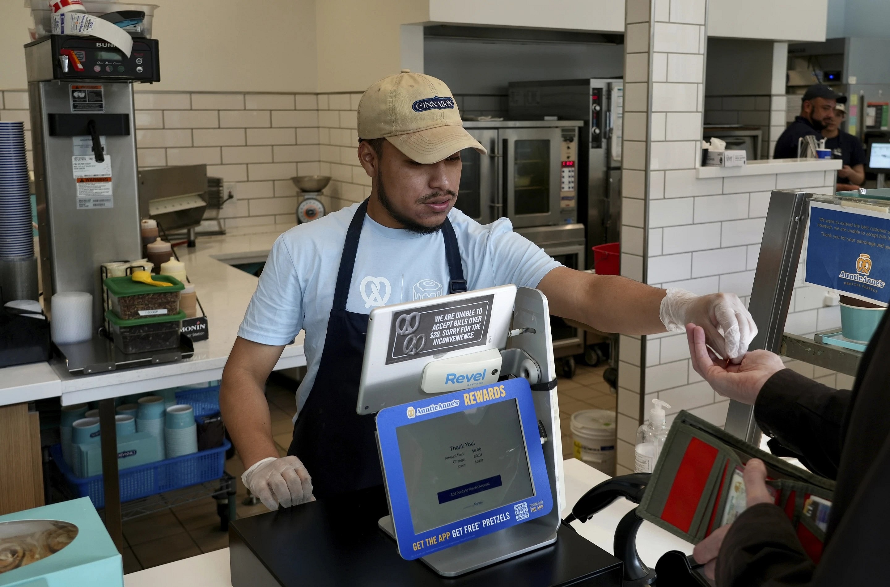 An employee wearing a yellow baseball cap, blue shirt and black apron hands change to a customer at a restaurant
