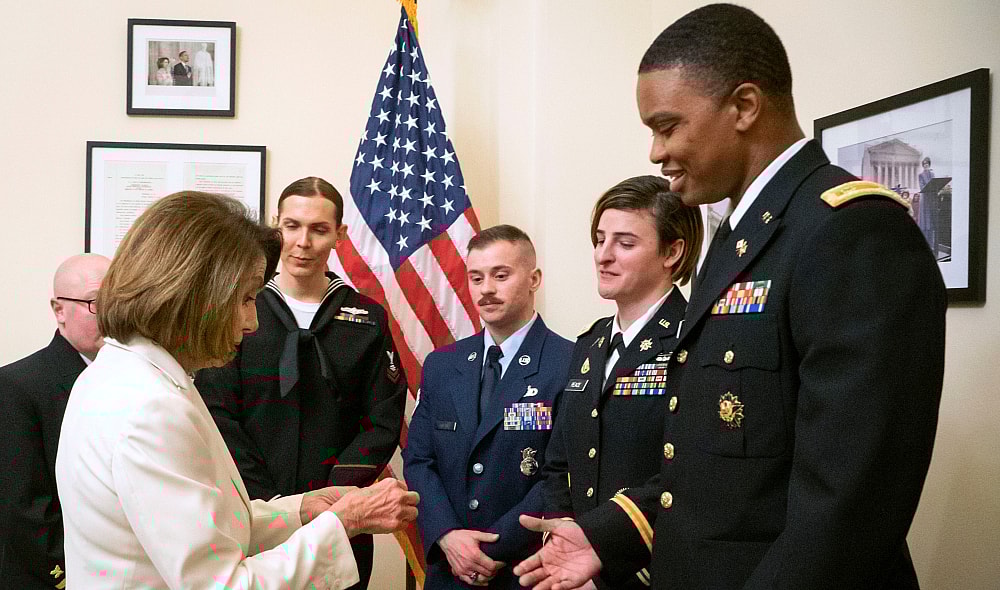In this Tuesday, Feb. 5, 2019 photo released by the her office, Speaker of the House Nancy Pelosi, D-Calif., left, gives challenge coins to U.S. Army Maj. Ian Brown, right, and other military service members to thank them for their service, in her office at the Capitol following the State of the Union address in Washington. Brown, 38, is a two-time Bronze Star recipient who transitioned from female to male while advising the Army's deputy chief of staff in operations and planning. (Julio Obscura/Office of the Speaker of the House Nancy Pelosi via AP)