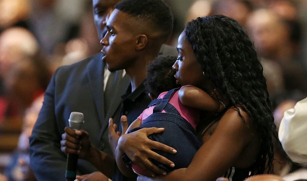 In this June 18, 2019 file photo Dravon Ames, holding microphone, speaks to Phoenix Police Chief Jeri Williams and Phoenix Mayor Kate Gallego, as his fiancee, Iesha Harper, right, holds 1-year-old daughter London, at a community meeting in Phoenix. Still stinging from national outrage sparked this summer by a videotaped encounter of officers pointing guns and cursing at the family, community members are holding low-key meetings aimed at helping Phoenix officials figure out how citizens could help oversee the city's officers. (AP Photo/Ross D. Franklin, File) thegrio.com