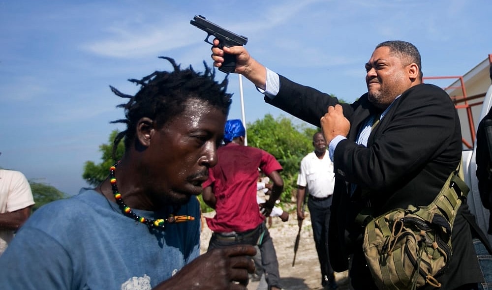 Ruling party Senator Ralph Fethiere fires his gun outside Parliament as he arrives for a ceremony to ratify Fritz William Michel's nomination as prime minister in Port-au-Prince, Haiti, Monday, Sept. 23, 2019. Opposition members confronted ruling-party senators, and Fethiere pulled a pistol when protesters rushed at him and members of his entourage. (AP Photo/Dieu Nalio Chery) thegrio.com