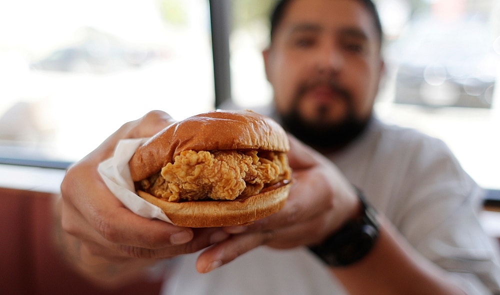 Randy Estrada holds up his chicken sandwiches at a Popeyes, Thursday, Aug. 22, 2019, in Kyle, Texas. A nation already polarized finds itself embroiled and divided once again, but this time, politics has nothing to do with it: The blame lays squarely on a fried piece of poultry.(AP Photo/Eric Gay) thegrio.com