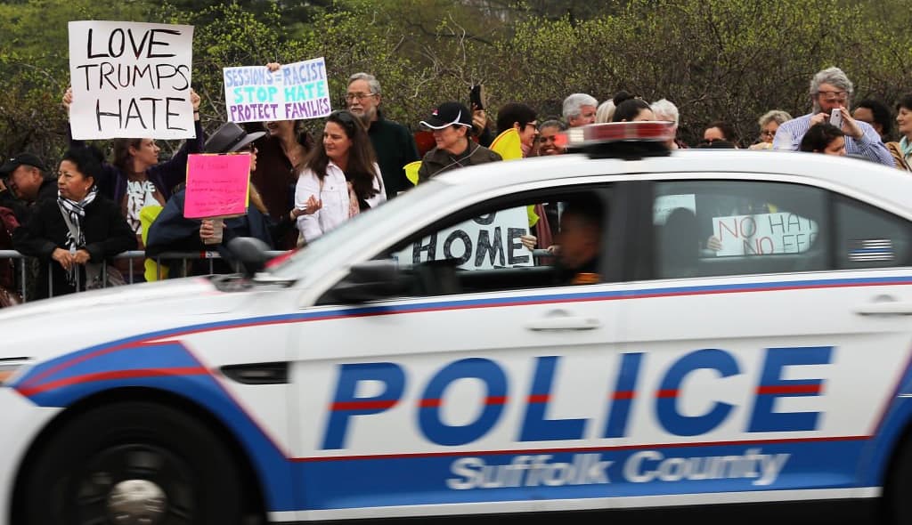 CENTRAL ISLIP, NY - APRIL 28: Police pass a group of protesters outside of the venue where Attorney General Jeff Sessions was to speak to local, state and federal law enforcement about a recent spate of gang related killings on April 28, 2017 in Central Islip, New York. Since the start of the school year the violent street gang MS-13 has been blamed for 11 deaths of mostly young people in residential Brentwood and neighboring Central Islip. The bodies have often been found in wooded areas and vacant lots. Sessions, who takes a tough stance on law and order, vowed to bring the gang leaders to justice. (Photo by Spencer Platt/Getty Images) thegrio.com