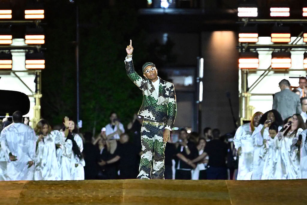 Louis Vuitton Men’s Creative Director Pharrell Williams points upward wearing a pixelated camouflage suit