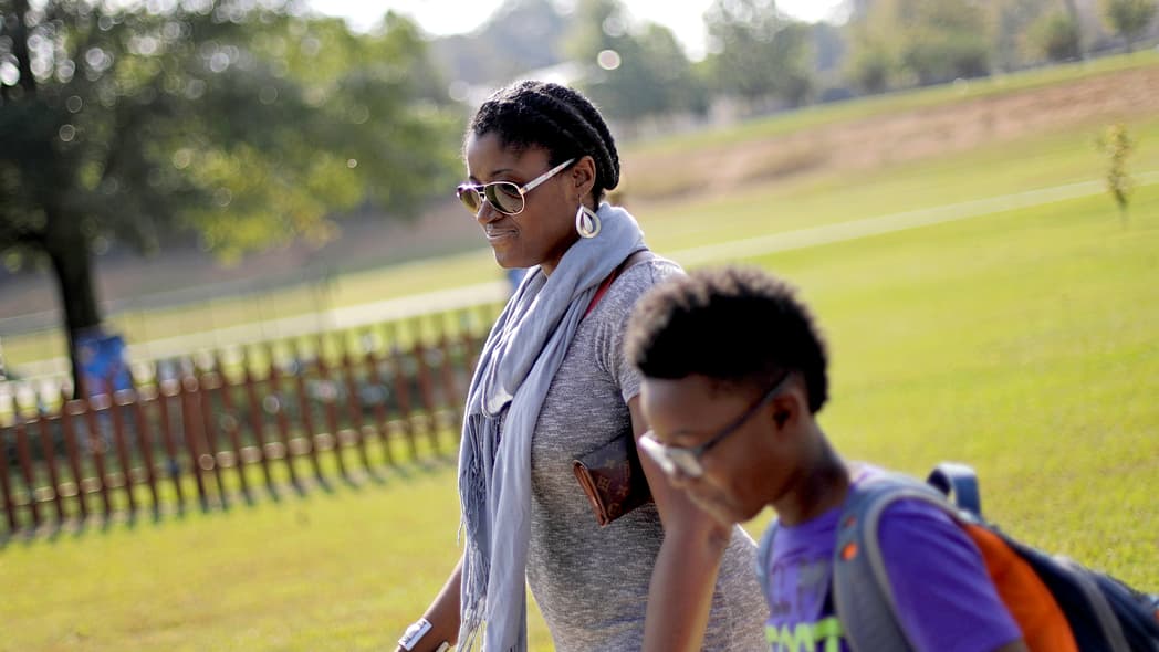 In this Oct. 11, 2017 file photo, Corrie Davis, left, picks up her son Turner from Big Shanty Elementary School in Kennesaw, Ga. The previous month, the school invited fifth-graders to dress up as characters from the Civil War. Davis says a white student dressed as a plantation owner approached her son and said "You are my slave." She requested that the school to stop the annual Civil War dress-up day. Recently, an investigation by New York Attorney General Letitia James found in May that a mock "slave auction" that singled out black students at the private Chapel School in Westchester County had a profoundly negative effect on all involved students. (AP Photo/David Goldman, File)