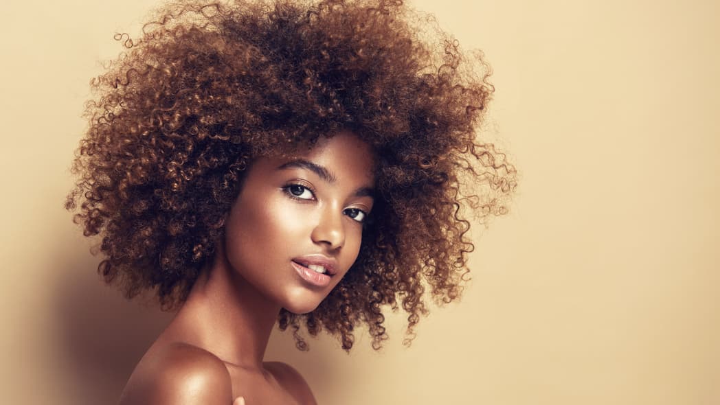 Beautiful black woman . Beauty portrait of african american woman with clean healthy skin on beige background. Smiling beautiful afro girl.Curly black hair thegrio.com