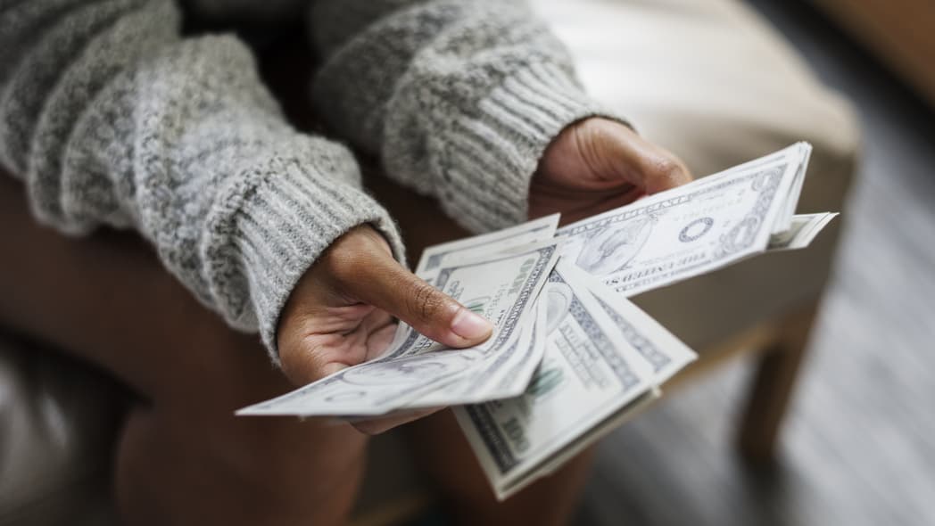 Black woman holds money, theGrio.com
