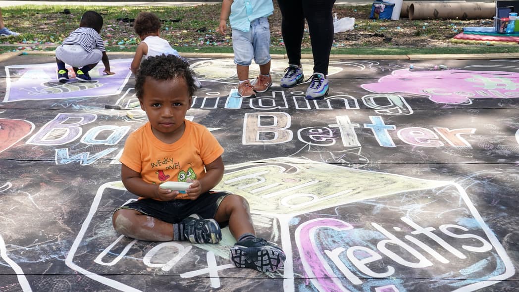 A child sitting on a chalk mural on the sidewalk