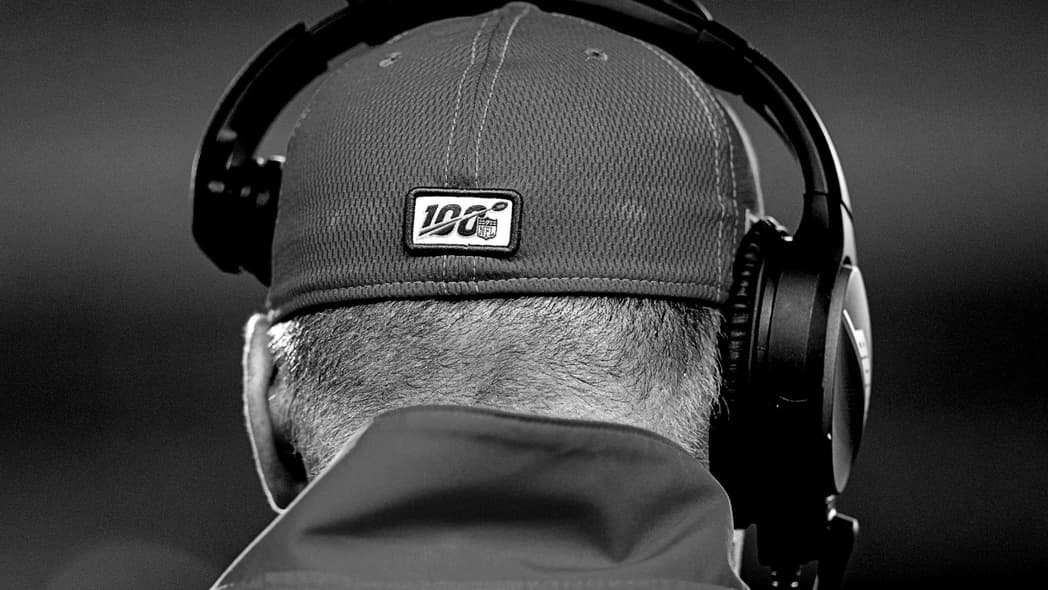 The back of a man's head wearing a baseball cap and headset