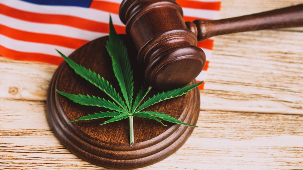 An American flag behind a gavel and a sound block with a marijuana leaf