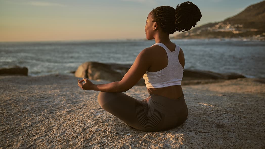 A woman sits in lotus position on a beach