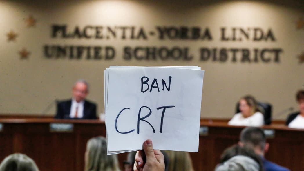 A hand holding a sign reading "Ban CRT"