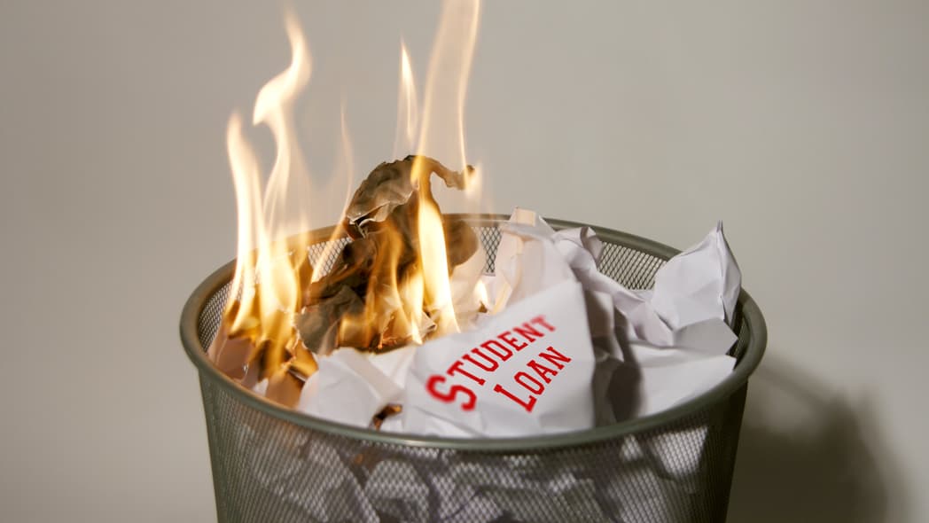 A paper reading "Student Loan" burning in a wastebasket