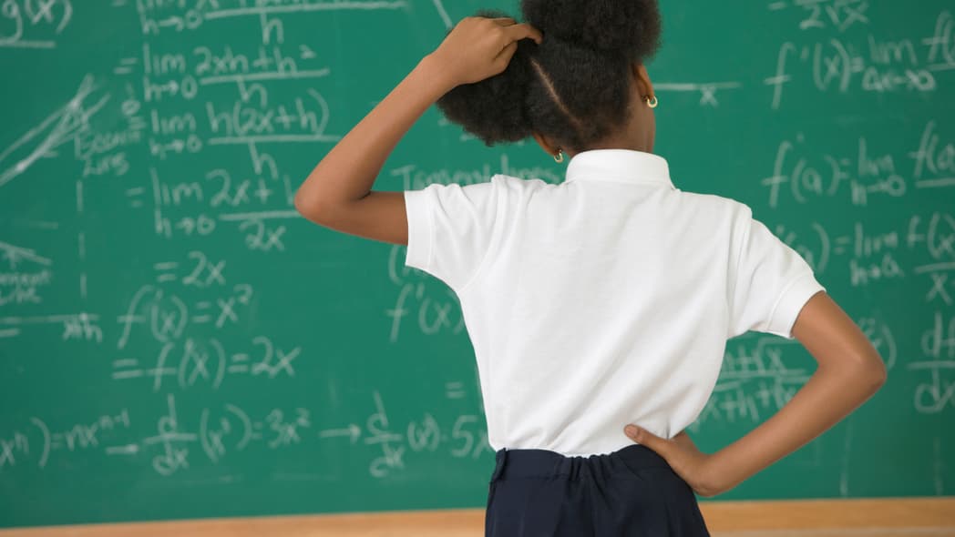 A girl stands at a chalkboard scratching her head