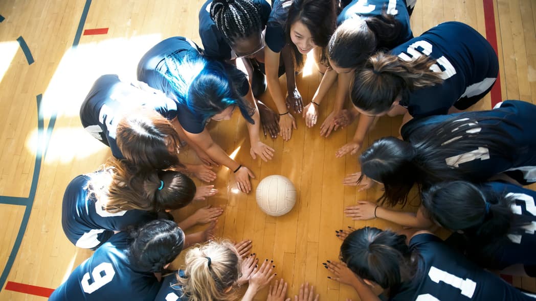 Young people kneel on a basketball court around a volleyball