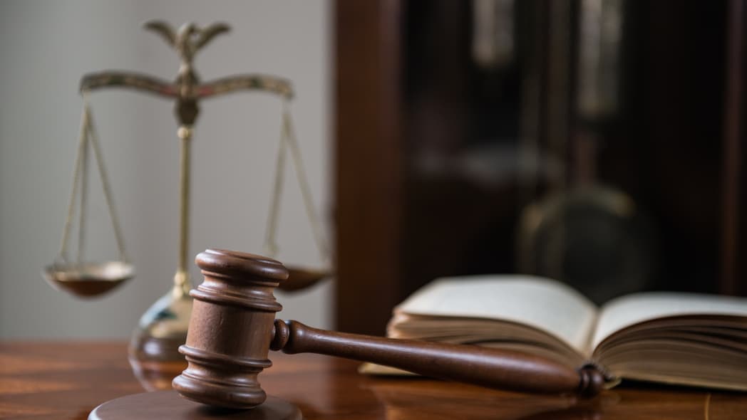 A wooden table displays a brown wooden gavel and sound block, an open book and a brass scale