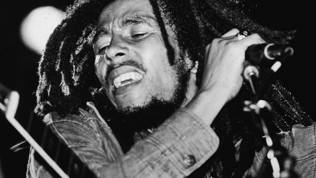 Black-and-white photo of the late Jamaican reggae musician Bob Marley on stage with a microphone in the late 1970s.
