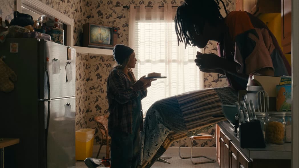 Actor Carmen Ejogo presents food on a plate to actor Jharrel Jerome as a giant