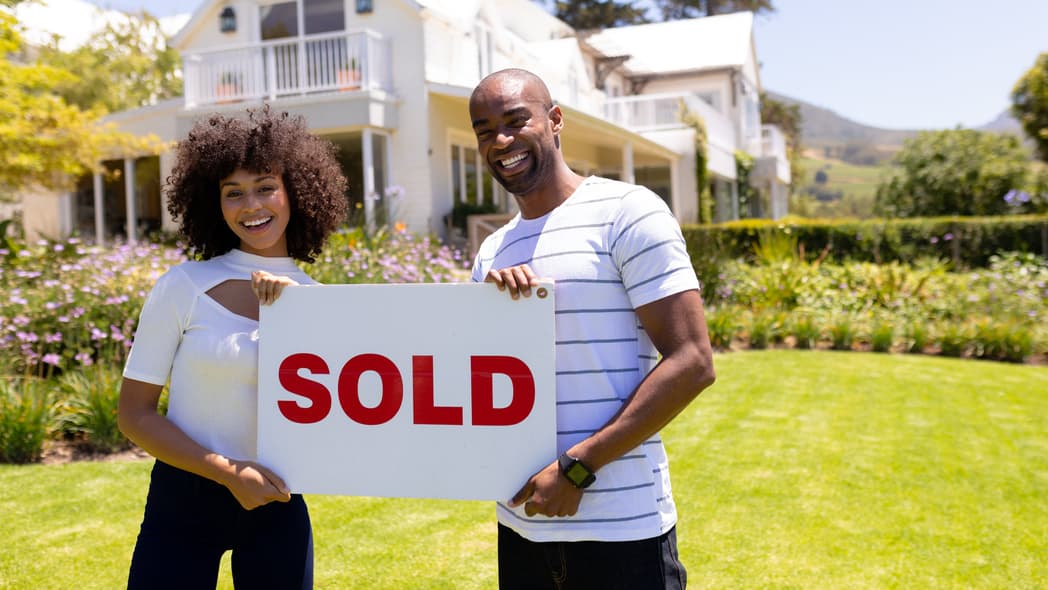 A couple in front of a house holding a "Sold" sign