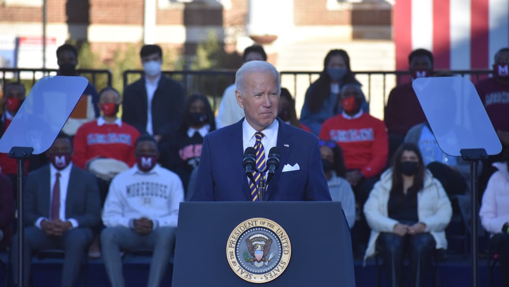 President Joe Biden in a blue suit and blue-and-yellow striped tie behind a podium