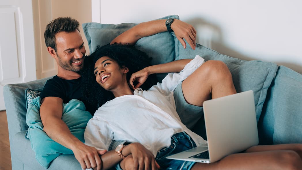 A couple lays together on a couch with a laptop
