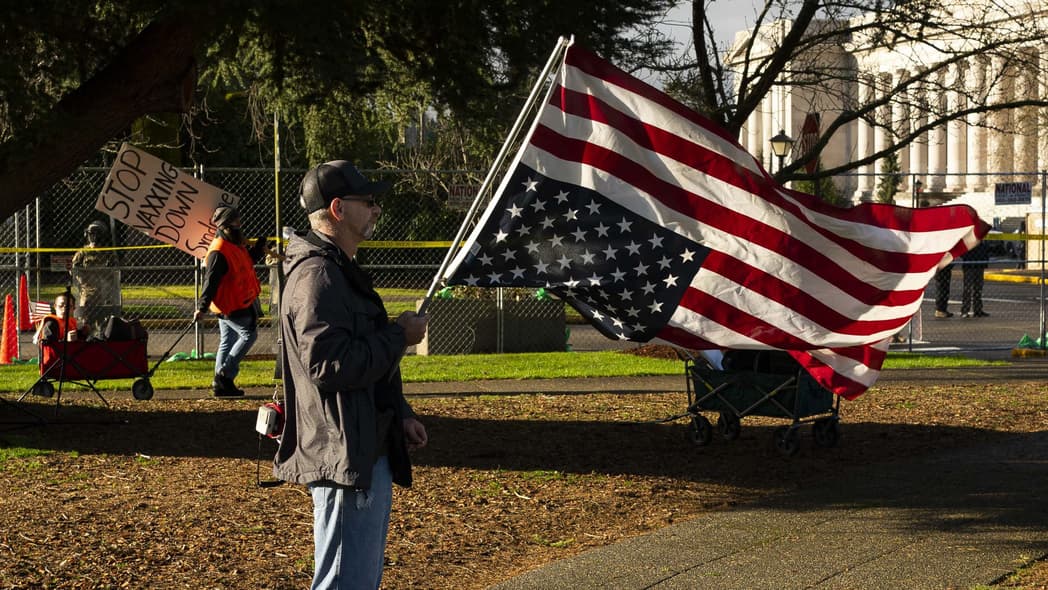 A conservative demonstrator holds a U.S. flag upside down as an anti-vaccination demonstrator walks nearby